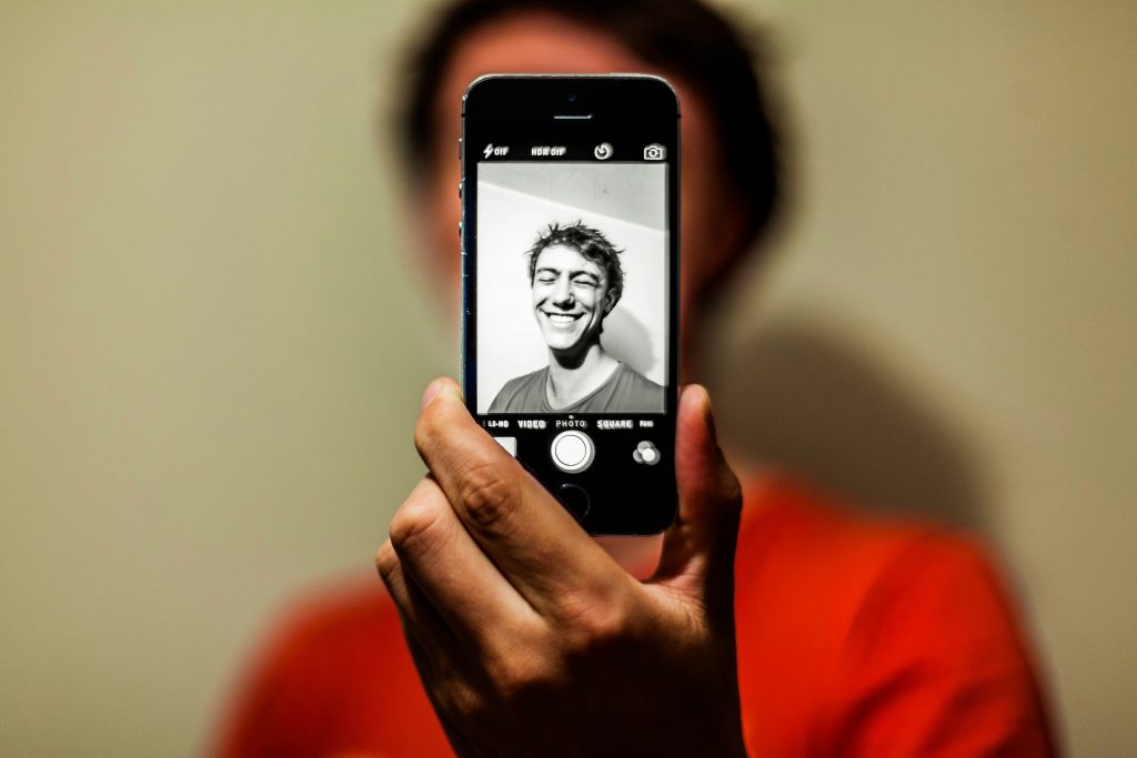 Closeup of a person's hand holding a smartphone displaying a smiling user's photo, with video, photo and other app menu options visible